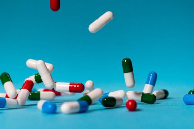 Renkli haplar mavi arka plana düşer. İlaçlar düşüyor. Mavi masadaki kırmızı, yeşil, mavi ve beyaz haplar.