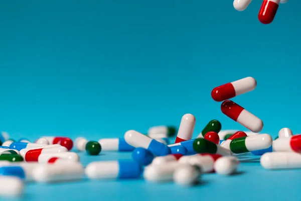 Colorful pills fall on a blue background. Medicines falling. Red, Green, Blue and white pills on a blue table