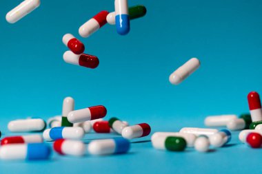 Renkli haplar mavi arka plana düşer. İlaçlar düşüyor. Mavi masadaki kırmızı, yeşil, mavi ve beyaz haplar.