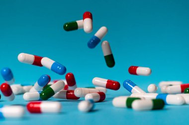 Renkli haplar mavi arka plana düşer. İlaçlar düşüyor. Mavi masadaki kırmızı, yeşil, mavi ve beyaz haplar.