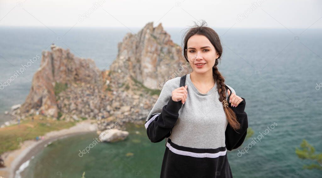 Tourist girl on the shore of lake Baikal against the background of Shamanka rock, Olkhon island.