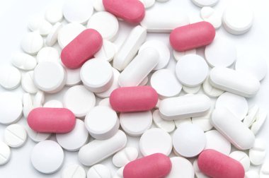 Reçeteli ilaçlar, haplar ve beyaz kapsüller ile pembe tabletler arasında farklı renklerde tabletler. Beyaz arka planda. Seçici odak. 
