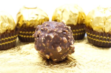 Ferrero Rocher, fındık ve lüks lezzetlerle dolu birinci sınıf çikolata topu tatlısı. Altın folyo arka planda İtalyan çikolata şekerleri.