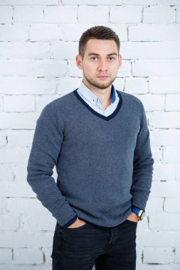 Beyaz tuğlalı duvara karşı gömlek ve süveter giyen genç adam.