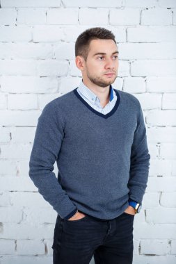 Beyaz tuğlalı duvara karşı gömlek ve süveter giyen genç adam.