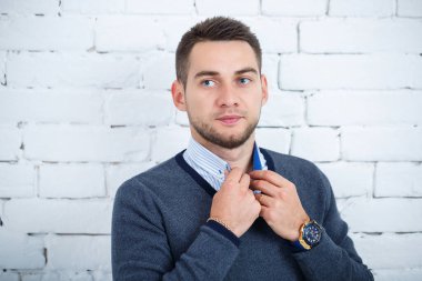 Beyaz tuğlalı duvara karşı gömlek ve süveter giyen genç adam.