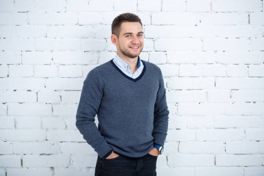 Beyaz tuğlalı duvara karşı gömlek ve süveter giyen genç adam.