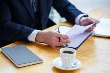 Yetişkin erkek akıl hocası, yönetmen, gözlüklü iş adamı ve masada otururken evrak okuyan bir takım elbise. Çalışma günü konsepti