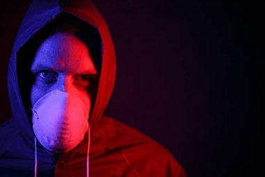 Maskeli ve kimyasal korumalı kırmızı ve mavi ışık altında bir adam. Virüse karşı savaş. COVID-19