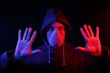 Koruyucu kauçuk giysili ve beyaz tıbbi maskeli bir adam. Virüs koruması. Kırmızı ve maviyle aydınlatılmış.