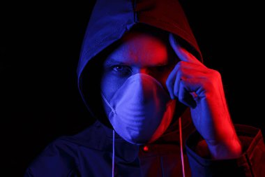 Koruyucu kauçuk giysili ve beyaz tıbbi maskeli bir adam. Virüs koruması. Kırmızı ve maviyle aydınlatılmış.