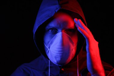 Koruyucu kauçuk giysili ve beyaz tıbbi maskeli bir adam. Virüs koruması. Kırmızı ve maviyle aydınlatılmış.