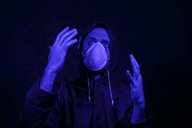 Koruyucu takım elbiseli ve karanlık bir odada beyaz maskeli bir adam. Cadılar Bayramı imajı. Virüs koruması. Renkli ışıklarla aydınlatılmış