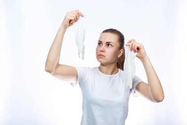 Kız ellerinde beyaz tıbbi eldiven tutuyor. Mikroplara ve virüse karşı koruma. Beyaz arka planda beyaz bir tişört giyiyor..