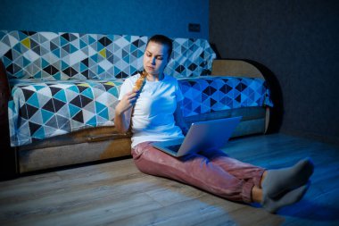 Beyaz tişörtlü bir kız karanlıkta kanepede oturur ve dizüstü bilgisayarında film izler. Kruvasan yer ve çay içer.