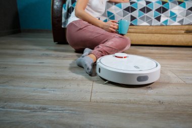 Ev halkı için modern teknolojiyle basit ve kolay bir temizlik. Kız çay içip dinlenirken elektrik süpürgesi evi temizliyor.