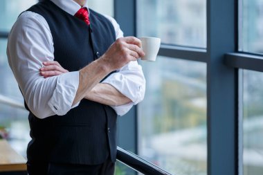 Gülümseyen mutlu yönetici, ofisinde elinde bir fincan kahveyle fotokopi alanı olan bir pencerenin arka planında dururken başarılı kariyerini düşünür.