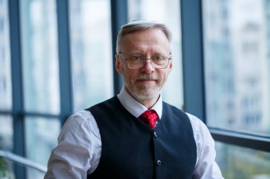 Gülümseyen mutlu yönetici, ofisinin arka planında fotokopi alanı olan bir pencerenin yanında dururken başarılı kariyerini düşünür.