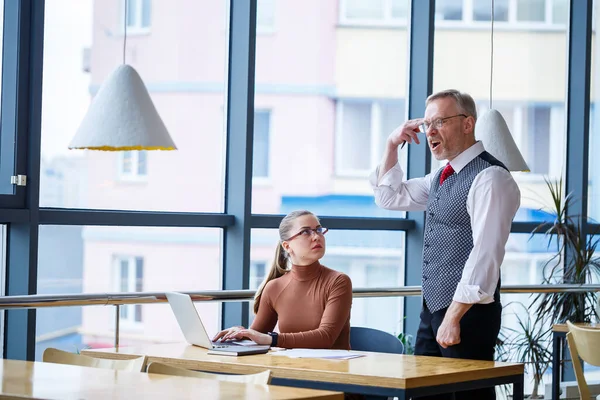 Girl business lady sitting at a wooden table with a laptop and working teacher boss mentor indicates her mistakes. School of a new business development concept.