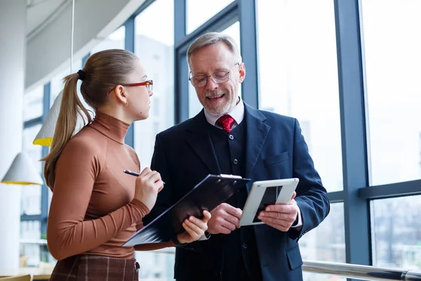 Man managing director tells his school subordinate about business development plans in his office near a large window