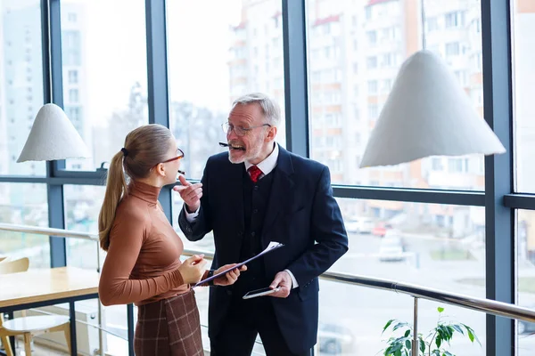 A male businessman and a woman sign a contract and celebrate success in his office. Hold pens in their teeth and smile