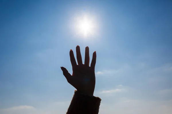 silhouetted a female hand against a blue sky and bright sun