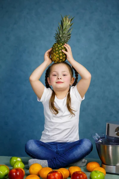 little girl in a white t-shirt loves fruits. She holds a pineapple in her hands