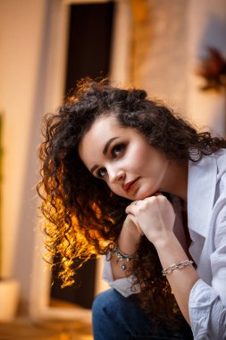 Bukleli güzel bir manken. Beyaz bir gömlek ve kot pantolon giyiyor..