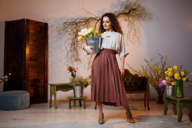 Bir kova lale taşıyan kıvırcık bir kızın portresi. Taze çiçekleri tutar ve güzel fotoğraflar çeker. Stüdyoda çiçekli parlak fotoğraflar.