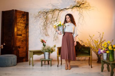 Bir kova lale taşıyan kıvırcık bir kızın portresi. Taze çiçekleri tutar ve güzel fotoğraflar çeker. Stüdyoda çiçekli parlak fotoğraflar.