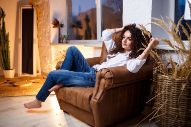 Bukleli güzel bir manken. Beyaz bir gömlek ve kot pantolon giyiyor..