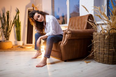 Bukleli güzel bir manken. Beyaz bir gömlek ve kot pantolon giyiyor..