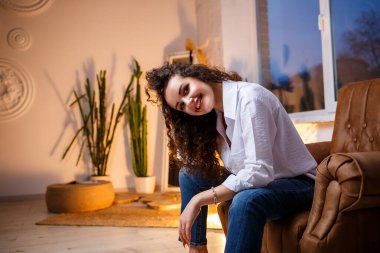 Bukleli güzel bir manken. Beyaz bir gömlek ve kot pantolon giyiyor..