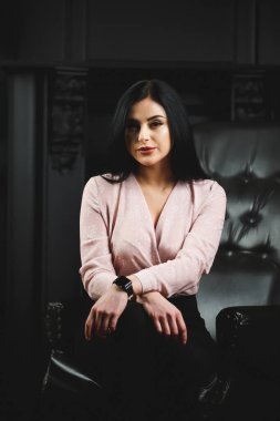 Siyah deri sandalyede açık renk bluzlu güzel bir kız.