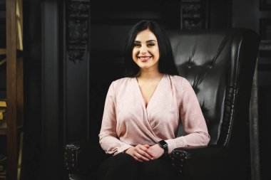 Siyah deri sandalyede açık renk bluzlu güzel bir kız.