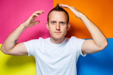 Çok renkli arka planda beyaz tişört giymiş genç, neşeli bir adamın portresi şık bir saç stili ve pozitif duygular yaratıyor.