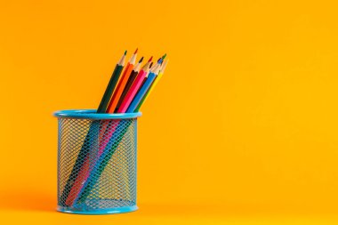 Turuncu arka planda ofis için renkli kalemlerle mavi metal kova.