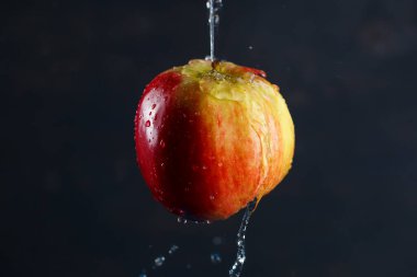 Kırmızı-sarı büyük elma, koyu arkaplanda suyla dolu.