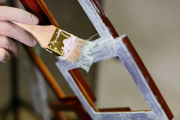 the master paints with a brush a wooden brown photo frame with light paint