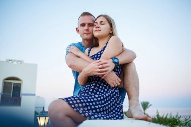 Denize ve palmiye ağaçlarına bakan büyük bir terasta bir adam ve bir kız.