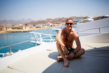 Başarılı adam deniz manzaralı beyaz bir yatta oturuyor. Kızıl deniz, parlak güneş