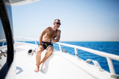 Şortlu ve gözlüklü bir iş adamı. Kızıl denizde beyaz bir yatta.