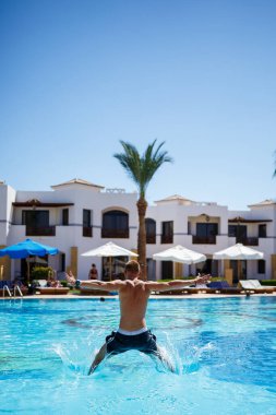 Şortlu adam, parlak güneşin altında havuzda banyo yapıyor.