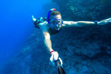 Maskeli ve şnorkeli olan bir adam Kızıl Deniz 'in mavi sularına dalıp kendini fotoğraflıyor.
