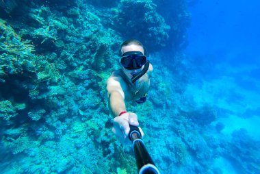 Maskeli ve şnorkeli olan bir adam Kızıl Deniz 'in mavi sularına dalıp kendini fotoğraflıyor.