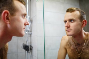 Bir adam aynanın önünde yüzünü jiletle traş eder. Deri tahrişi. Banyo prosedürü