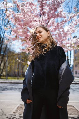 Uzun dalgalı saçlı, gri paltolu, spor ayakkabılı, sokakta dönen genç, narin bir manken. Bahar ağaçları kadın gülüyor ve neşe içinde koşuyor.