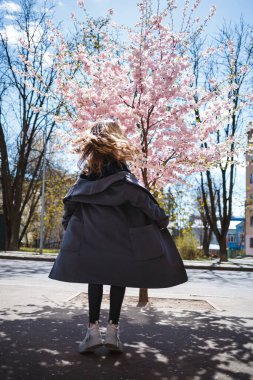 Uzun dalgalı saçlı, gri paltolu, spor ayakkabılı, sokakta dönen genç, narin bir manken. Bahar ağaçları kadın gülüyor ve neşe içinde koşuyor.