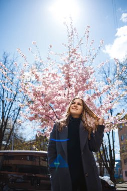 Şehrin sokaklarındaki ağaçta çiçeklerle sakura dalları. Şık bir kadın elinde çiçekli sakurayla sokakta dikiliyor. Modern, modaya uygun bir kız. Sakura ağacı çiçek açar..
