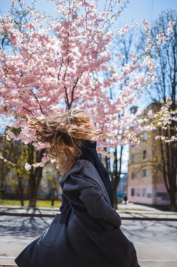 Uzun dalgalı saçlı, gri paltolu, spor ayakkabılı, sokakta dönen genç, narin bir manken. Bahar ağaçları kadın gülüyor ve neşe içinde koşuyor.